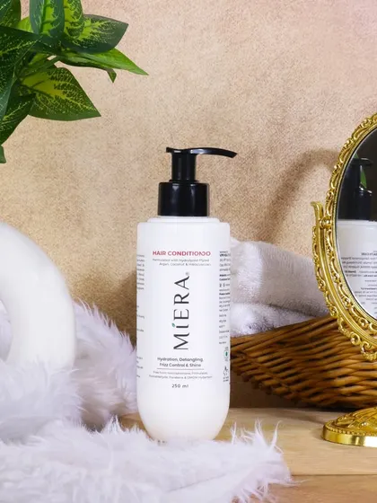 A luxurious bathroom setting for a hair conditioner. The gold mirror, fluffy textures, and soft lighting create a pampering, high end spa vibe for the product.