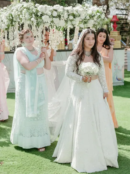 The bride's beautiful entry at her cross-cultural wedding, walking down a grassy aisle under a floral canopy.