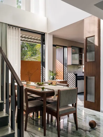 **The Glow House, Ahmedabad:** Sunlight from the side garden illuminates the dining space, connecting it to the outdoors. The material palette, including the striking green marble floor, was chosen to reflect and amplify the natural light, making the home feel bright and airy.