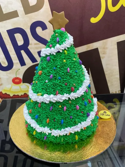 A festive 3kg cake sculpted into a Christmas tree with green piping and colorful sprinkle ornaments.