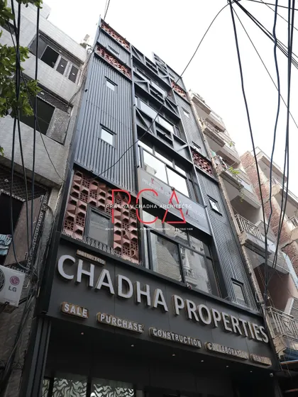 The Chadha Properties office facade in daylight, showing the contrast between the dark ACP louvers and the earthy terracotta jaalis.
