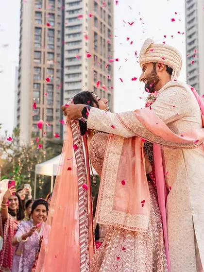 The groom lovingly places the varmala on his bride, surrounded by cheering family and a shower of rose petals. A moment of pure happiness.