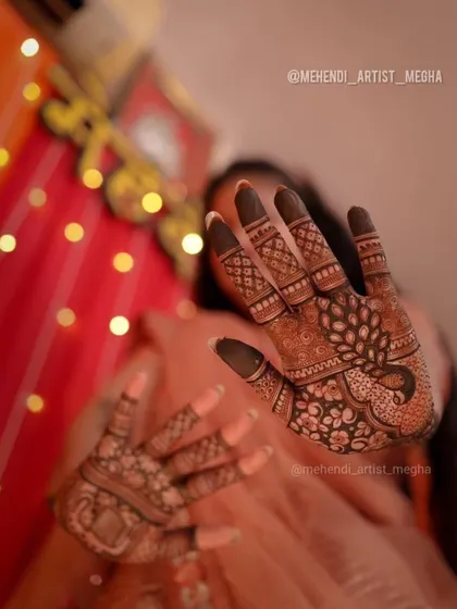 A creative shot focusing on the intricate peacock mehendi on the palm, with the festive lights in the background adding to the celebratory mood.