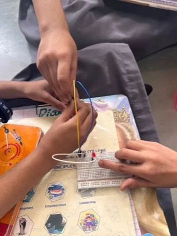 A close-up of students' hands as they carefully connect jumper wires to a breadboard, a fundamental skill in learning electronics and prototyping.