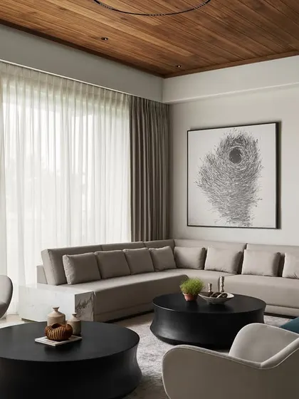 Natural light floods the living room, highlighting the contrast between the soft, neutral furnishings and the bold, organic shapes of the black concrete coffee tables. The entire composition is designed to feel both relaxing and refined.