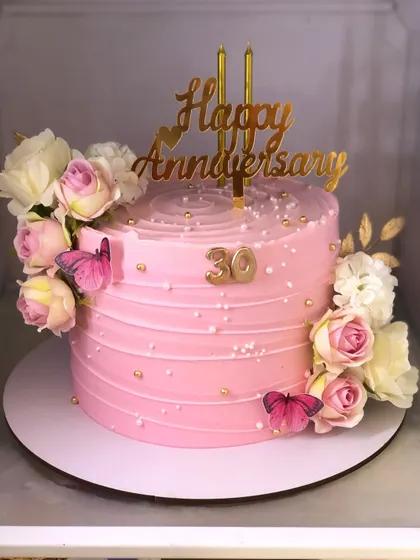 A pretty pink anniversary cake, decorated with fresh roses, edible butterflies, and a golden "30" to mark the milestone.