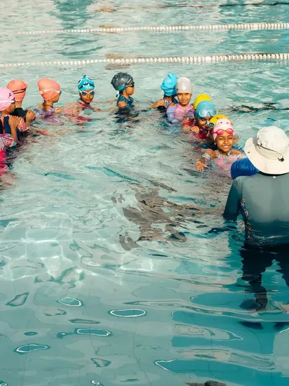 Group lessons are a great way for kids to learn from both the coach and each other. An instructor gathers a class of young swimmers in the water for a group activity, fostering teamwork and social skills.