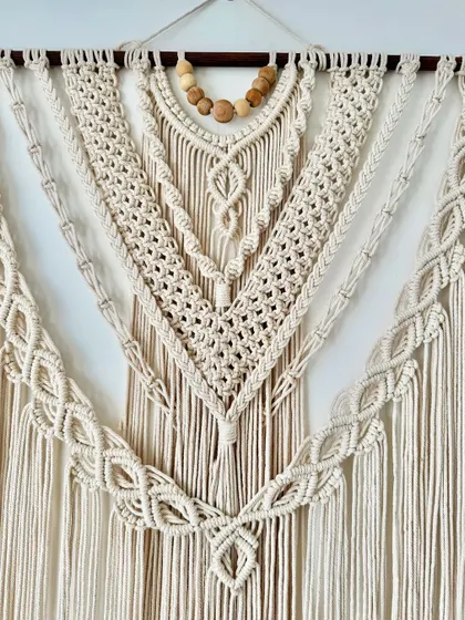A close-up of the intricate knotting on this large, natural-colored wall hanging, featuring beautiful wooden beads at the top.