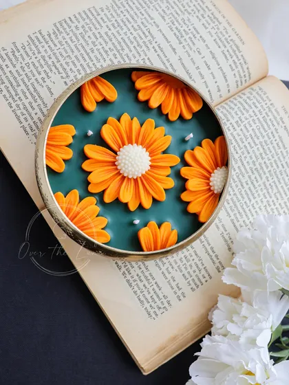 A single tangerine orange and emerald green Daisy Urli, placed on an open book. It shows how my candles can be used as beautiful decorative objects to style any corner of your home.