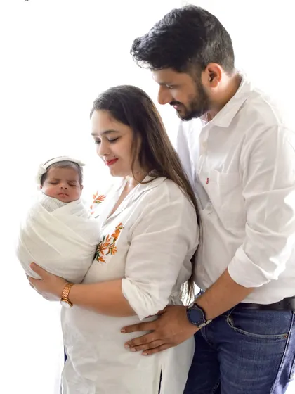 A lovely standing portrait of a new family. The mother holds the baby while the father stands behind, creating a sense of unity and support.
