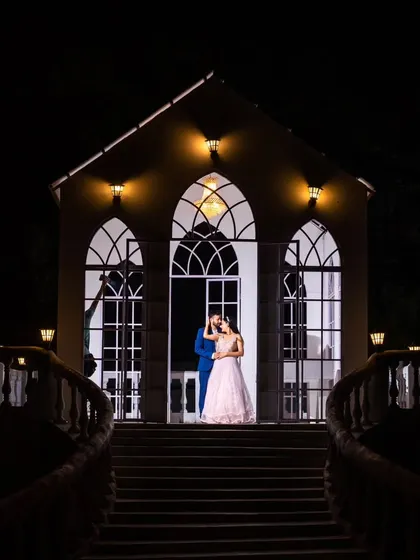 A wider view of the enchanting night scene. The lighting on the building creates a magical, almost theatrical, backdrop for this romantic couple portrait.