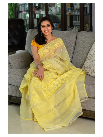 A light and airy portrait featuring a handwoven Dhakai Jamdani saree. The natural pose and home environment make this a perfect shot for a brand that emphasizes comfort and elegance.