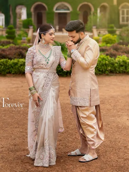 A classic, chivalrous pose. The groom, in his elegant pastel sherwani and dhoti, kisses his bride's hand, capturing a moment of pure romance.