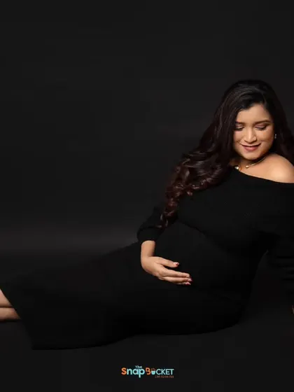 A simple, elegant portrait of the mom-to-be in a classic black off-the-shoulder dress. The dark backdrop and focused lighting create a moody and sophisticated feel.