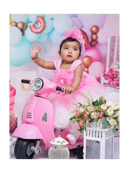 Waving hello from her pink scooter, this little girl is the star of her 'Candy Land' themed portrait. The pastel balloons and sweet treat props complete this vibrant setup.