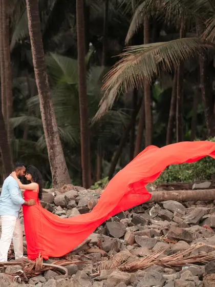 A romantic moment amidst the palm trees. The vibrant red trail of her gown creates a stunning contrast with the natural surroundings, perfect for a beach pre-wedding shoot.