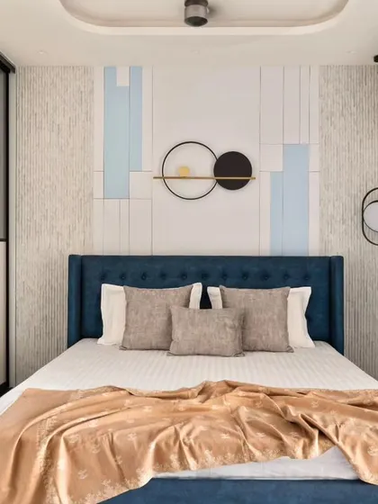 The son's bedroom in the same project uses a cool blue palette. The headboard wall features geometric paneling, and the floor-to-ceiling wardrobe has a clean, modern design that conceals a hidden dresser.