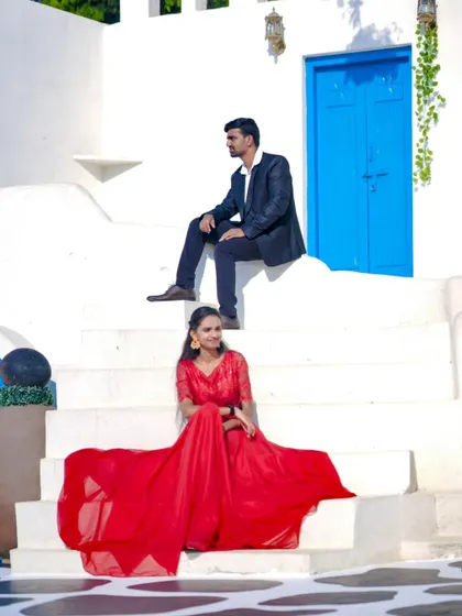 A beautiful pre-wedding photo with the bride-to-be in a stunning red gown, posing on the steps of a Santorini-themed set.