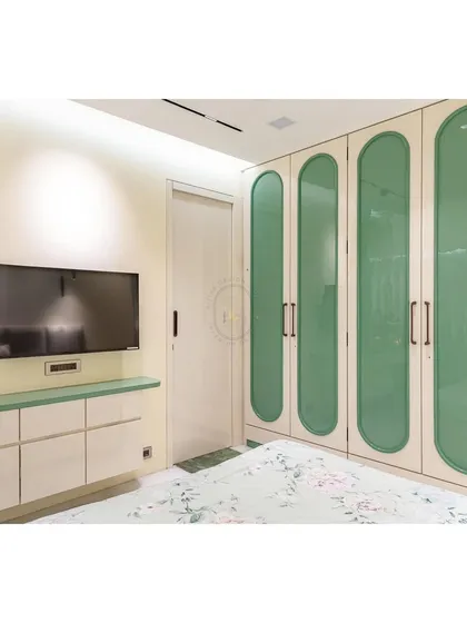 This image showcases the custom-designed wardrobe with unique capsule-shaped green glass panels. This feature adds a distinct personality to the room while the glass allows for a subtle glimpse of the contents inside.