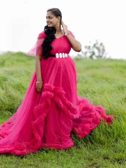 A solo portrait in a field of green, showcasing the dramatic, long trail of the pink ruffle gown.