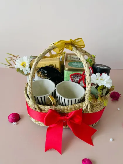 The bright red ribbon adds a festive pop of color to this charming Kauna basket, filled with mugs, tea, and other delightful items.