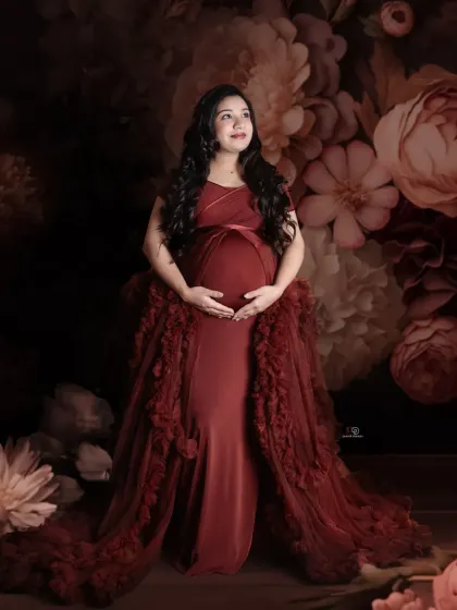 A beautiful portrait against a dark floral backdrop, this mom-to-be glows in a rich red gown. The dramatic lighting and elegant pose create a truly memorable maternity image.
