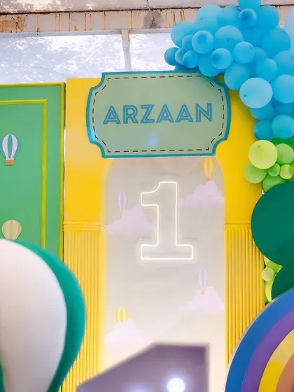 A close-up of the hot air balloon party backdrop, featuring a personalized name sign, a neon number '1', and a colorful rainbow prop.