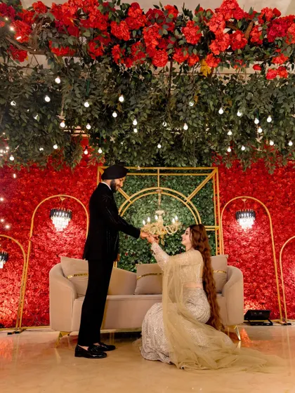 A romantic moment as the groom-to-be helps his fiancée, captured under a canopy of flowers and lights.