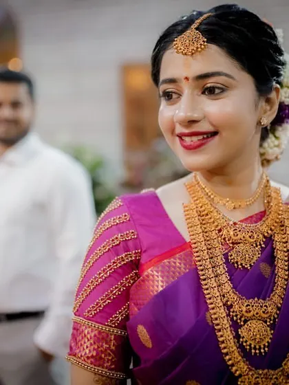 A beautiful portrait of the bride, her stunning gold jewelry and radiant smile taking center stage, with her groom softly focused in the background.