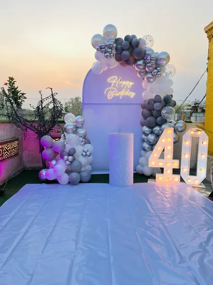 A 40th birthday party on a terrace. This setup features a purple backdrop, a silver and grey balloon arch, and large marquee numbers.