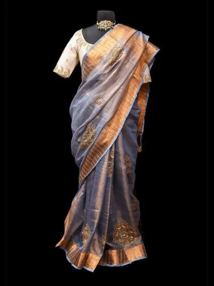 A mannequin draped in a grey organza saree with gold embroidery. This shows the beautiful structure and sheen of the fabric, making it a great choice for formal events.