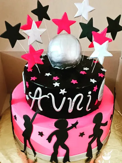 A groovy two-tiered disco theme cake with a silver disco ball and dancing silhouettes, perfect for a party.