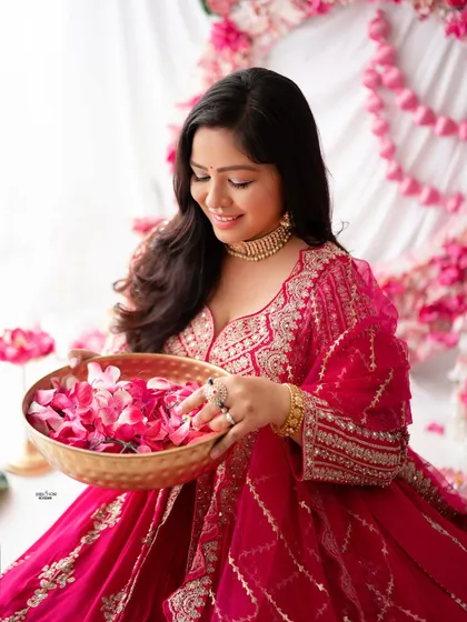 A beautiful portrait of a mother-to-be in a traditional pink outfit, holding a bowl of flower petals. The setup is rich with color and cultural aesthetics.