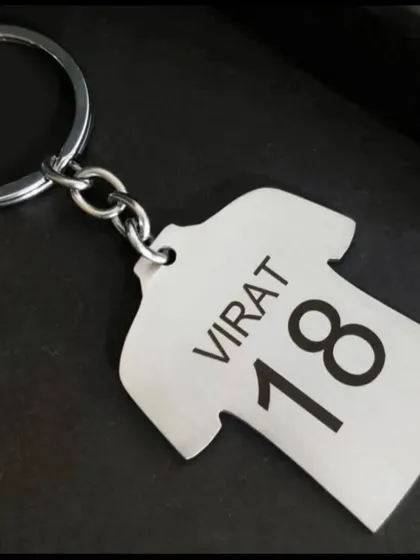 A great gift for any cricket fan, this metal keychain is shaped like a jersey. I can customize it with any name and number, like this 'Virat 18' example.