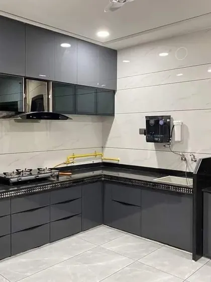 A sleek and modern kitchen with glossy dark grey cabinets and a black countertop. The handleless design and white tiled walls create a clean, high-contrast look.