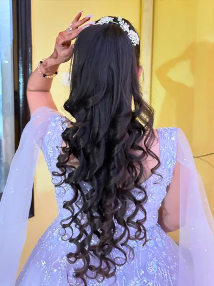 The back view of a party hairstyle, featuring a half-updo with a crystal accessory and long, defined curls.