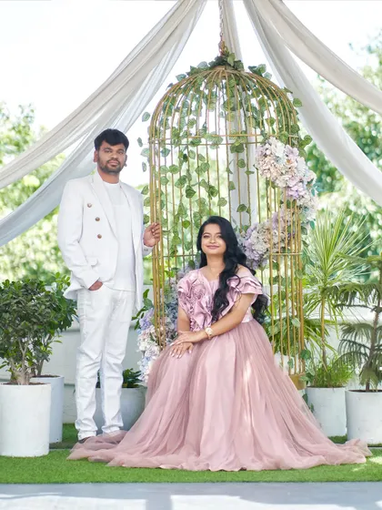 A full-length portrait of the couple in our studio's garden setup. The groom's all-white outfit is a perfect match for the bride's soft pink gown.