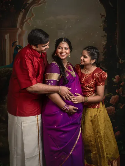 An expecting mother smiles radiantly as her husband and daughter embrace her. This image beautifully captures the love and excitement of a family waiting to welcome a new member.