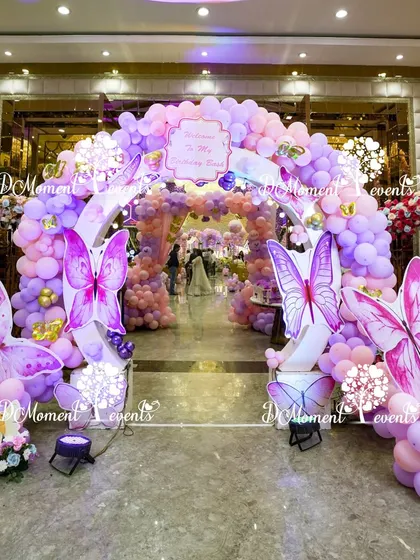 A grand entrance arch for a butterfly-themed party, featuring massive butterfly props and a lush arrangement of purple and pink balloons.