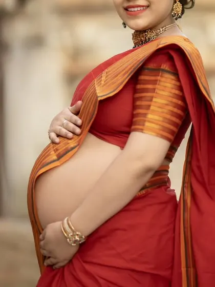 A close-up shot focusing on the baby bump, beautifully framed by the traditional red saree. This style is perfect for celebrating the baby's arrival in a culturally rich way.