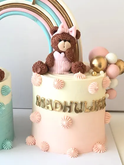 The matching pink teddy bear cake for the baby girl twin, featuring a pink bow and balloon details.