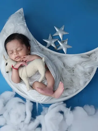 Drifting off to sleep on a soft, crescent moon. This setup uses a blue backdrop and fluffy clouds to create a dreamy, celestial atmosphere for a peaceful newborn portrait.