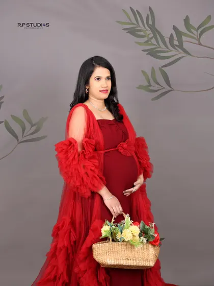 A classic maternity pose. The mom-to-be holds a basket of flowers, adding a touch of rustic charm to her elegant red gown.