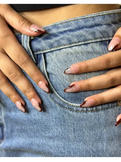 A simple yet classy design. This look features a sheer nude base with a thin, v-shaped French tip in a deep brown, creating a modern and minimalist effect.