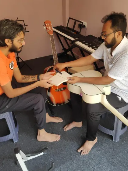 Guidance and growth. A moment of mentorship as knowledge is passed from teacher to student, helping with the finer points of guitar maintenance.
