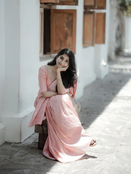 A full-length portrait that captures a moment of quiet grace. Seated on a bench in a serene, sunlit alley, this image has a timeless, classic feel.
