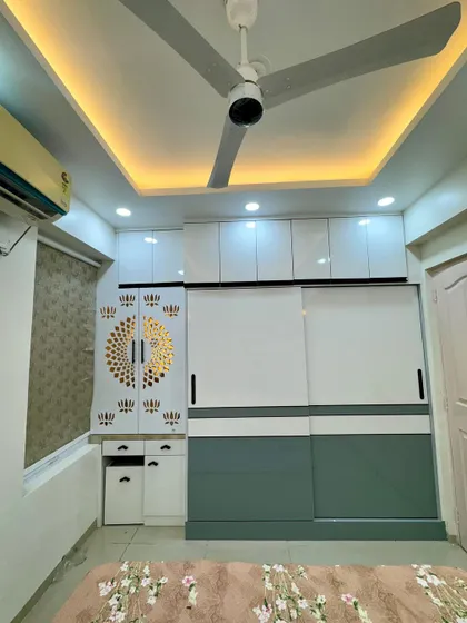 A bedroom featuring a large sliding wardrobe in white and green. We also integrated a small mandir unit with a beautiful CNC cut door.