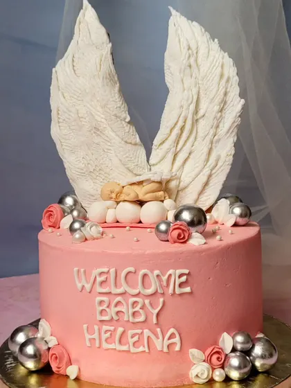 A beautiful baptism cake for Baby Helena. The design features a sleeping baby nestled between two large, detailed angel wings made of chocolate.