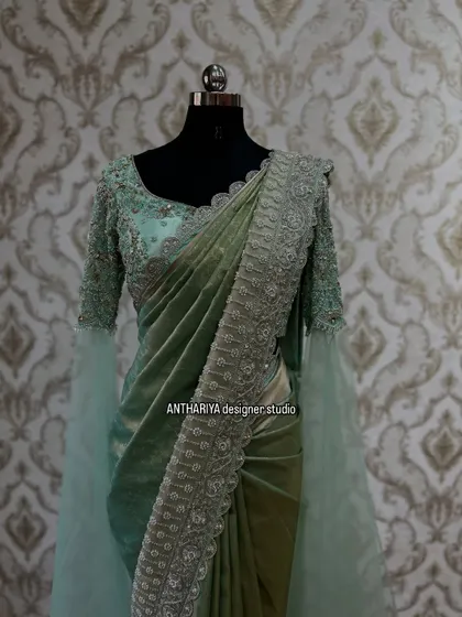A stunning pre-draped saree gown in a pastel green shade, with heavy embroidery on the blouse and dramatic flared sleeves.