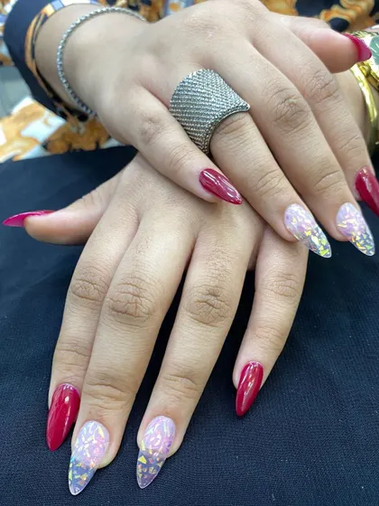 A bold and glamorous nail set featuring stiletto extensions. The design combines a deep red polish with translucent nails filled with sparkling butterfly glitter, showcasing a creative and dramatic style.